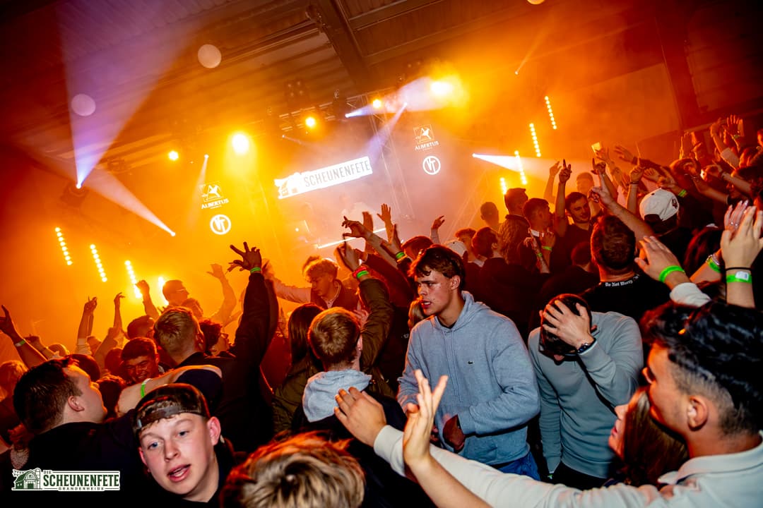 Volle Tanzfläche in orangem Licht vor der Bühne der Scheunenfete 2026
